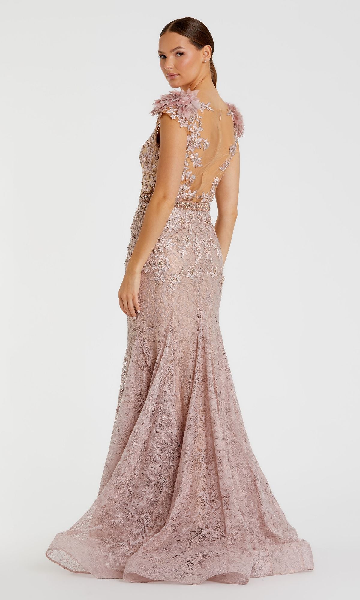 A woman wearing the Mac Duggal 79368 cap-sleeve, floor-length pale pink formal gown with floral appliqué and a sheer back stands facing slightly away from the camera.